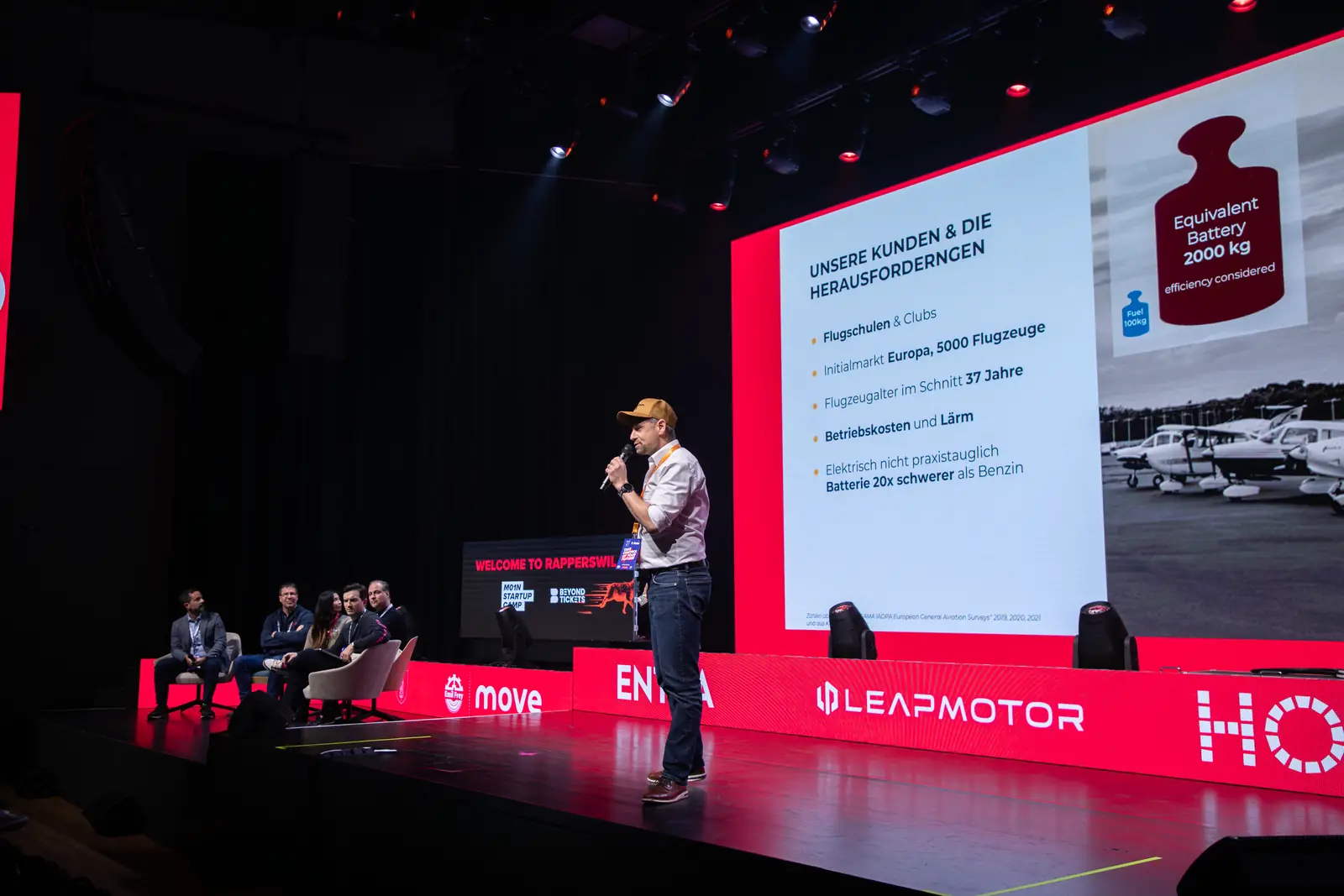 A founder pitches his aviation startup on the M01N Main Stage, the jury listens on the left